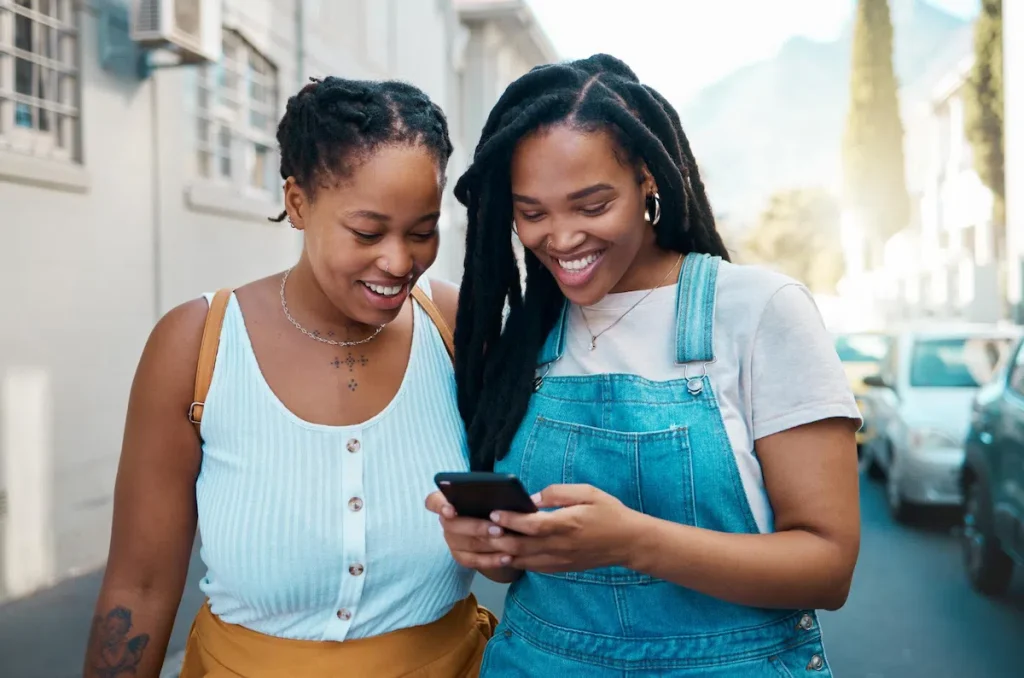 Two women smiling while checking loan approval on a smartphone