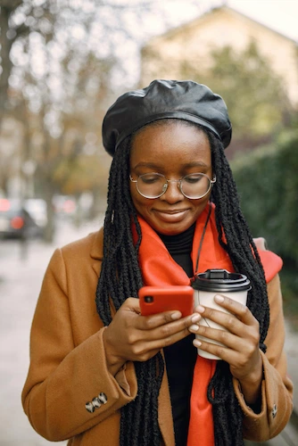 Smiling young woman in a tan coat and red scarf reviews an application for a payday loan in California on her mobile phone