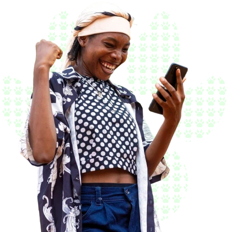 Smiling woman wearing a headband and patterned shirt looks at her phone and raises her fist in excitement.