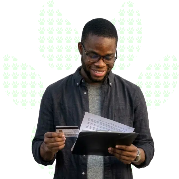 A smiling young man wearing glasses looks over documents in one hand holding a card in the other